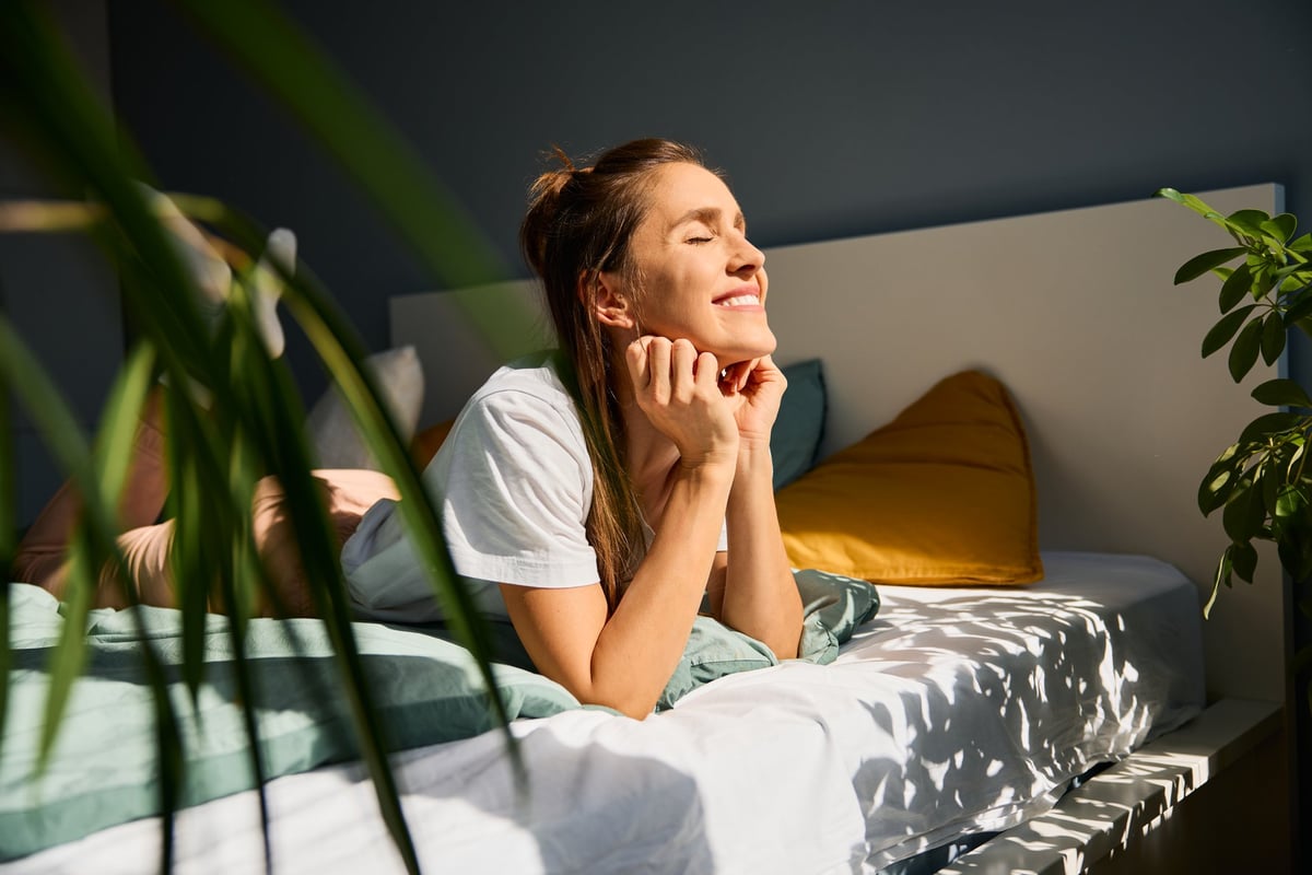 Woman resting in soft morning light with a warm drink and heat pack, considering supplements for period cramps