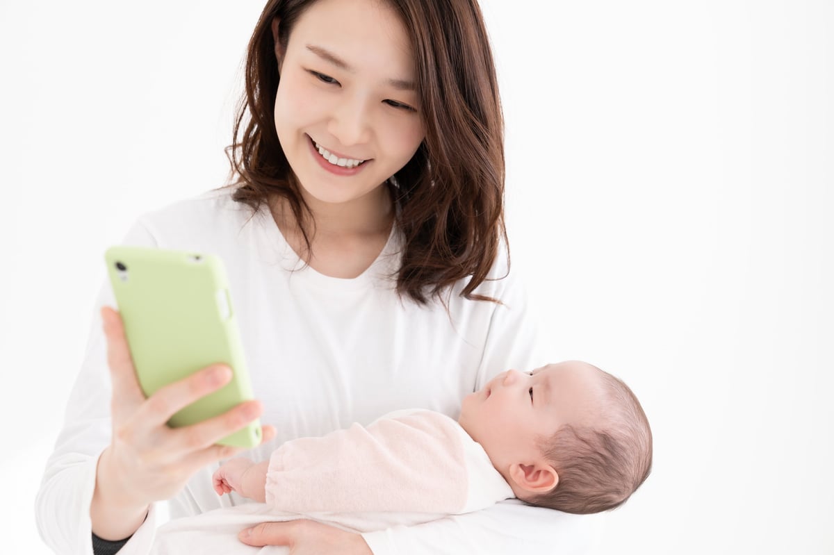 A new mother at home with her baby nearby, calmly tracking her cycle on her phone