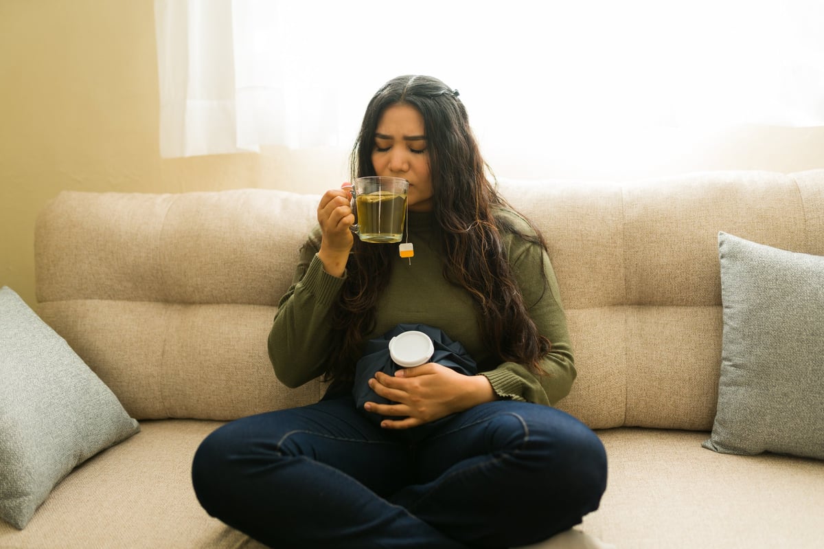 Woman using a heat pack on her lower belly at home, one of the period cramp treatments supported by evidence