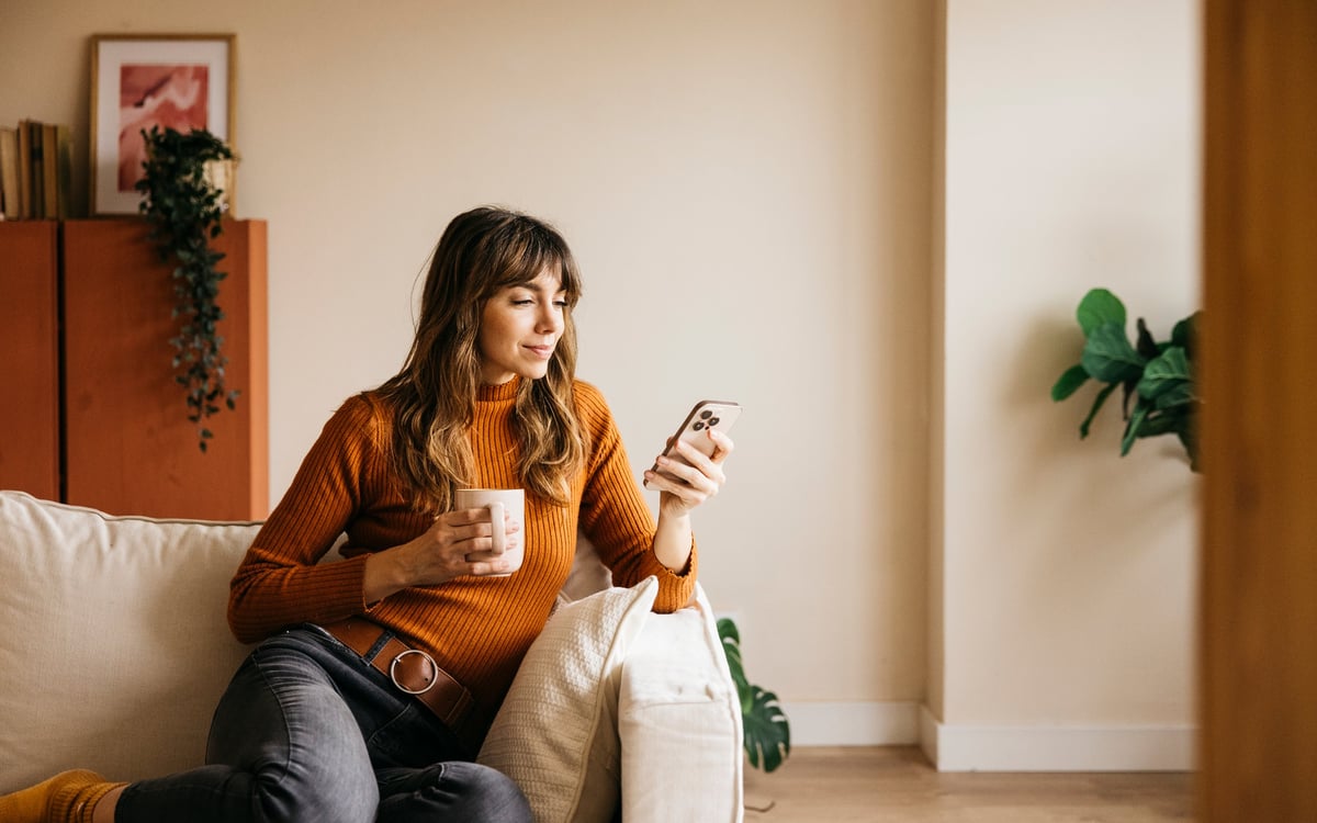 A woman relaxes on the sofa with a warm drink, tracking her cycle symptoms to better understand her mood