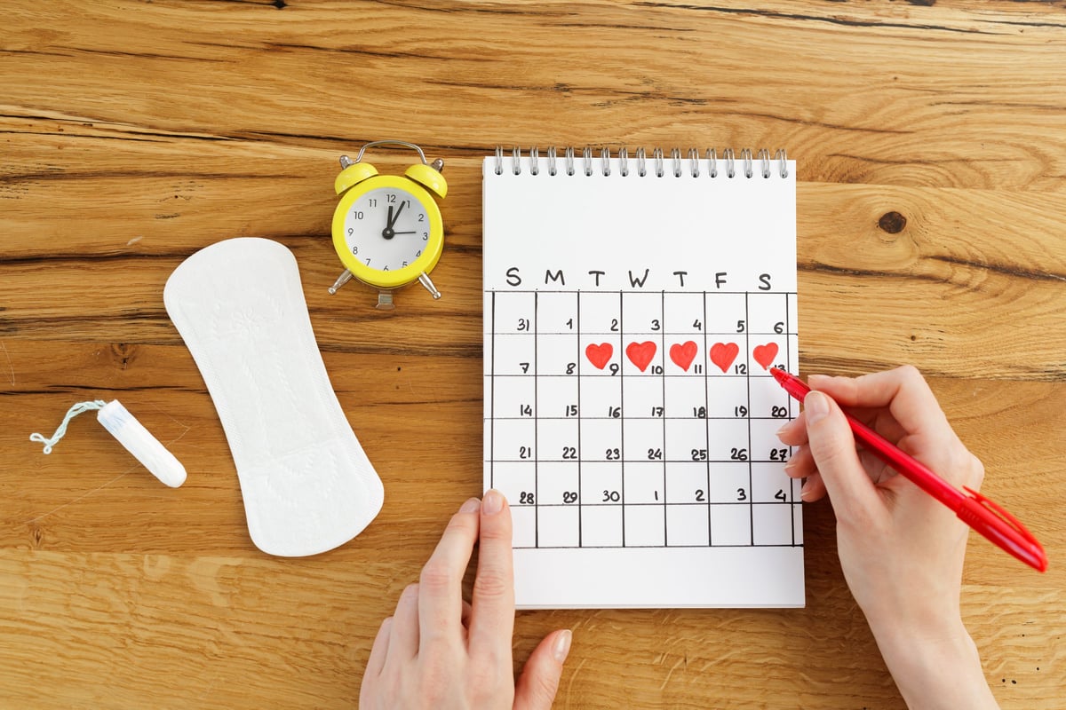 A woman calmly marks her menstrual cycle on a calendar with period products nearby